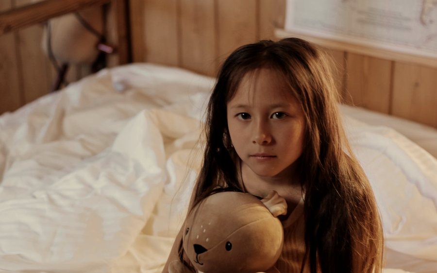 Une enfant serrant une peluche dans son lit.