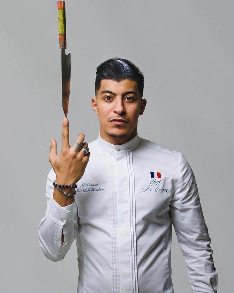 Mohamed Si Abdelkader en veste de chef, tenant un couteau.