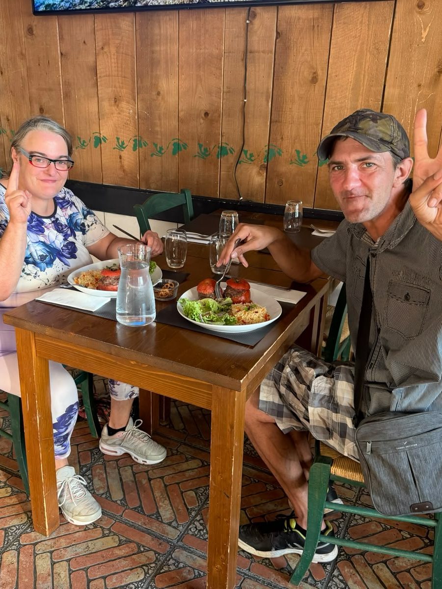 Deux personnes attablées au restaurant, souriantes, faisant le signe de la victoire.